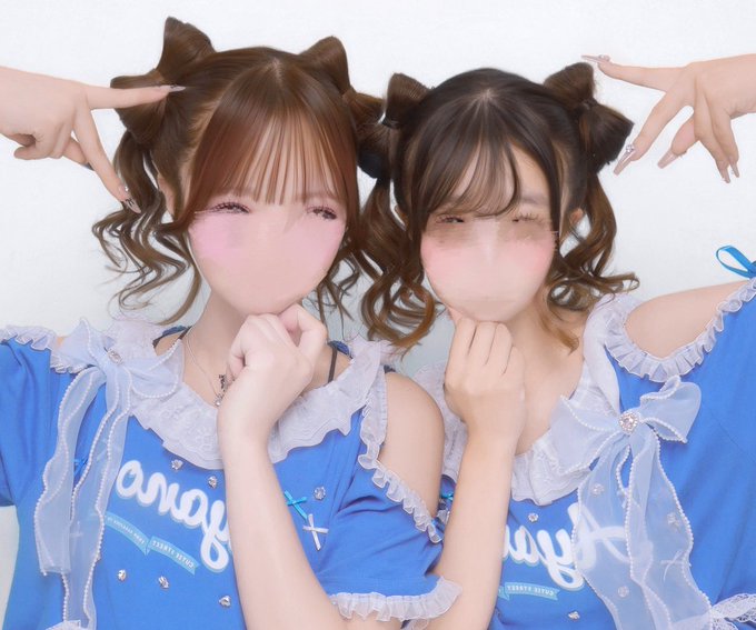 Two women pose together with matching blue outfits featuring white ruffles and cat-ear headbands, their faces blurred.