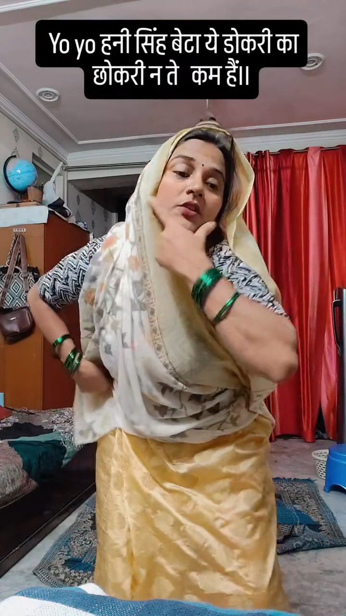 A woman wearing a yellow sari and dupatta dances in a room with red curtains. Hindi text overlays the video: 'Yo yo हनी सिंह बेटा ये डोकरी का डोकरी न ते कम है।।'