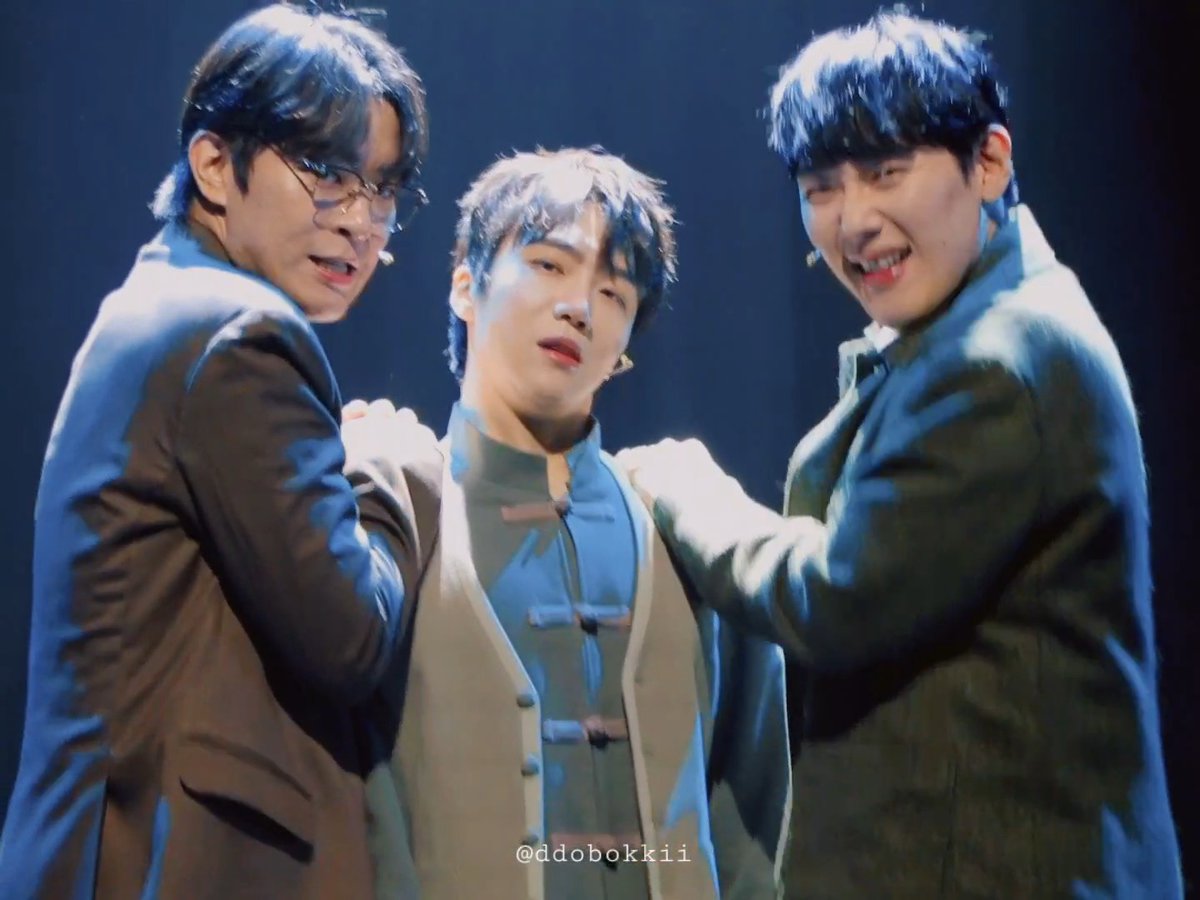 Three young male performers on stage in formal attire, with the watermark "@ddobokkii" visible at the bottom.