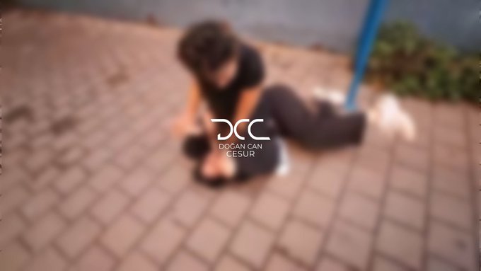 A blurry overhead shot shows a person with dark hair wearing black clothing sitting on a tiled surface, possibly tending to someone lying beside them, with a blue pole visible nearby. A watermark in the center reads "DCC - DOĞAN CAN CESUR," and the image appears to be a private, low-quality surveillance-style capture connected to the post's reference to Olaya.