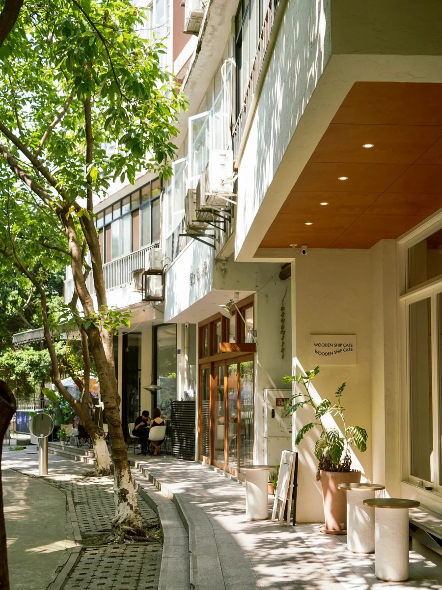 Reikotr33's tweet photo. Un rincón de la ciudad atrapado en un momento casual, el sol ilumina la tienda de flores con sus colores vivos, y un transeúnte pasa despacio, creando una escena tranquila y auténtica. https://t.co/coDmQaI19U