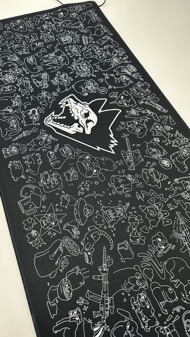 A black mat or fabric features white line-drawn doodles of various objects and creatures, with a large dinosaur logo in the center.