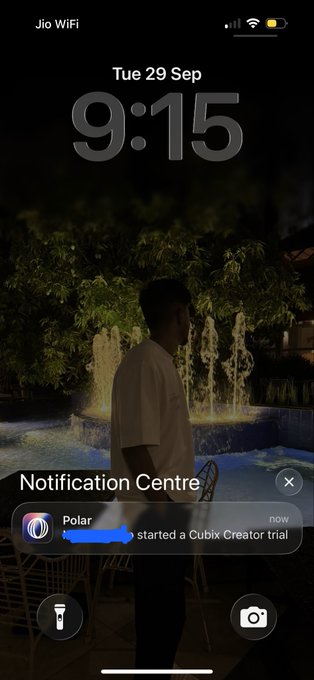 An iPhone lock screen showing the time '9:15' on 'Tue 29 Sep' over a dim wallpaper of a person standing by a pool, with a 'Polar' notification stating it started a Cubix Creator trial.