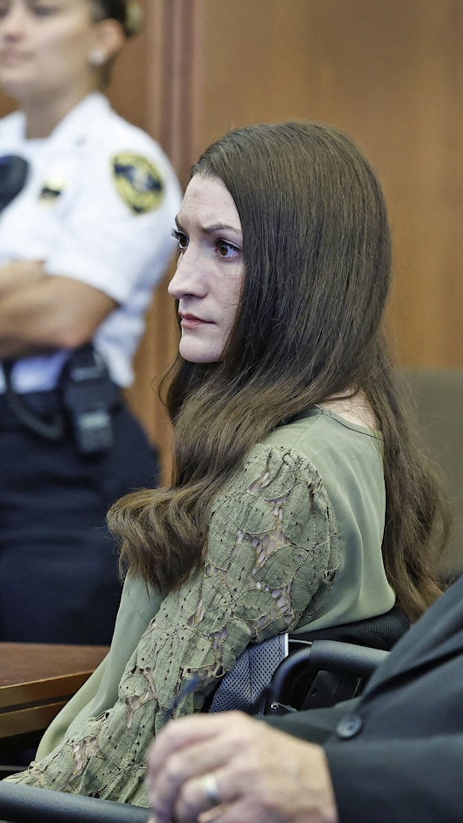 A solemn woman with long brown hair wearing a distressed green top sits in a wheelchair in what appears to be a courtroom, with a uniformed officer visible in the background. The image is associated with the Lindsay Clancy case, as referenced in the accompanying post about a holdout juror discussing the children's role in the proceedings.