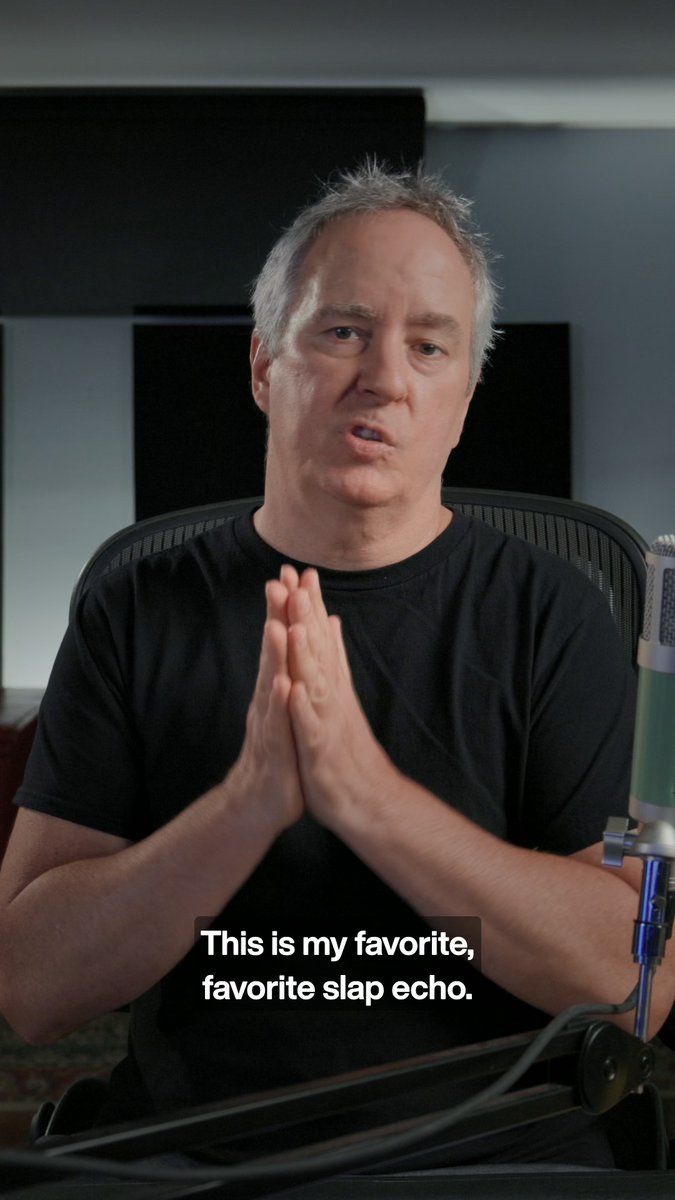 A man in a black t-shirt with grey hair sits at a desk with a microphone, hands clasped together, with the caption 'This is my favorite, favorite slap echo.'