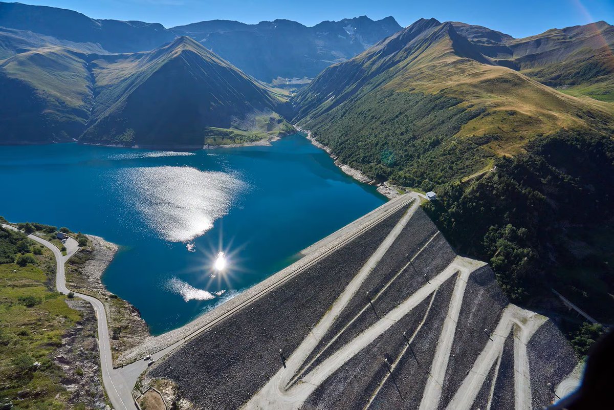 CeJourHistoire's tweet photo. La centrale la plus puissante de France passe ses heures creuses à remonter de l'eau dans une montagne.

Elle s'appelle Grand'Maison, elle est en Isère. 1 800 MW installés, selon EDF, soit 9 % de toute la puissance hydraulique du groupe.

Tout tient dans deux lacs.

En haut, à plus de 1 700 mètres d'altitude, le lac de Grand'Maison, retenu par un barrage de 140 mètres de haut et 560 de long. Environ 140 millions de mètres cubes.

En bas, 900 mètres plus bas, le lac du Verney et ses 15 millions de mètres cubes.

Aux heures creuses, quand l'électricité est abondante et que la demande dort, douze machines pompent l'eau du bas vers le haut.

Aux heures de pointe, quand la France allume ses plaques et ses fours, on ouvre.

L'eau retombe de 900 mètres et traverse les turbines. Trois minutes environ pour passer de zéro à pleine puissance, selon EDF.

EDF compare les 920 MW de sa station de Montézic à un réacteur nucléaire. Grand'Maison en pèse deux, et les livre en trois minutes.

Le rythme est commandé par le petit lac, pas par le grand. 15 millions de mètres cubes en bas : c'est ce plafond-là qui borne chaque cycle.

Le chantier a duré de 1978 à 1985. Premier groupe couplé au réseau fin 1985, installation complète fin 1987.

L'électricité qui arrive chez vous ce soir peut venir d'une eau remontée dans cette montagne quelques heures plus tôt.

Le site se visite, avec le musée EDF Hydrelec, à Vaujany.

Vous saviez qu'on stockait de l'électricité avec de l'eau ?