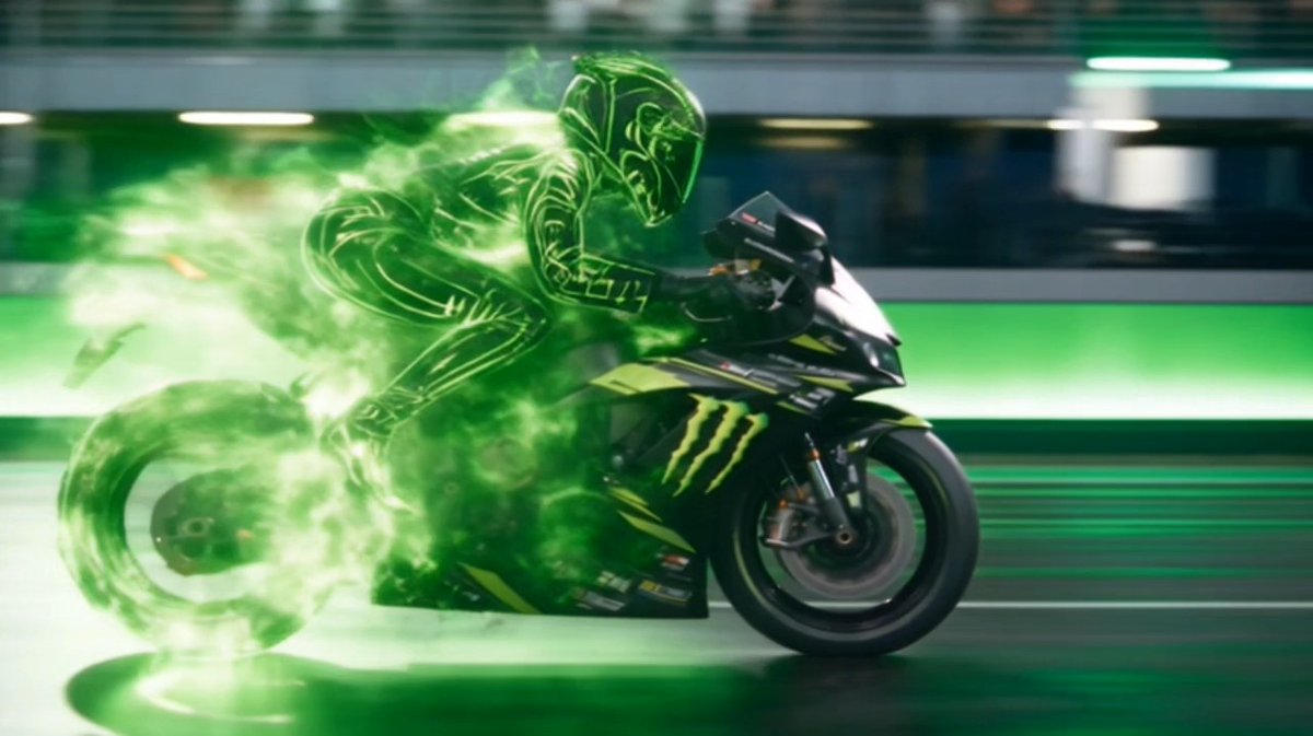 A dramatic action shot of a motorcycle racer dissolving into green glowing energy/smoke trails while riding a Monster Energy-branded sportbike.