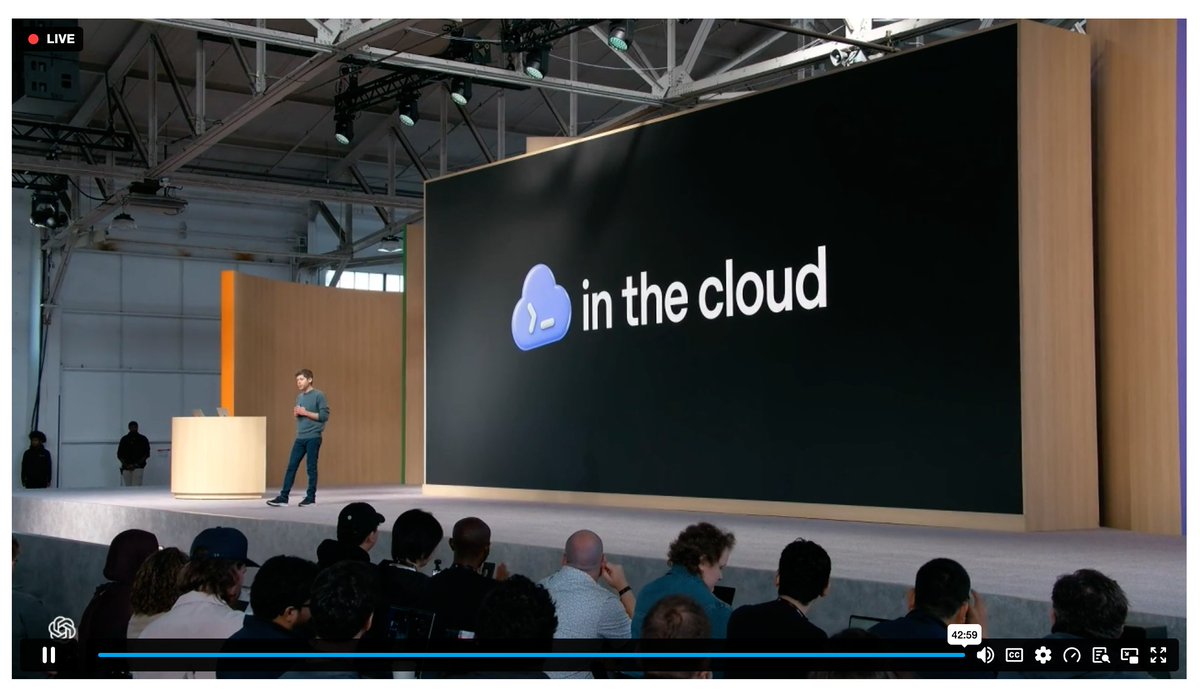 A man standing on a stage in front of a large screen with the words "in the cloud" on it.