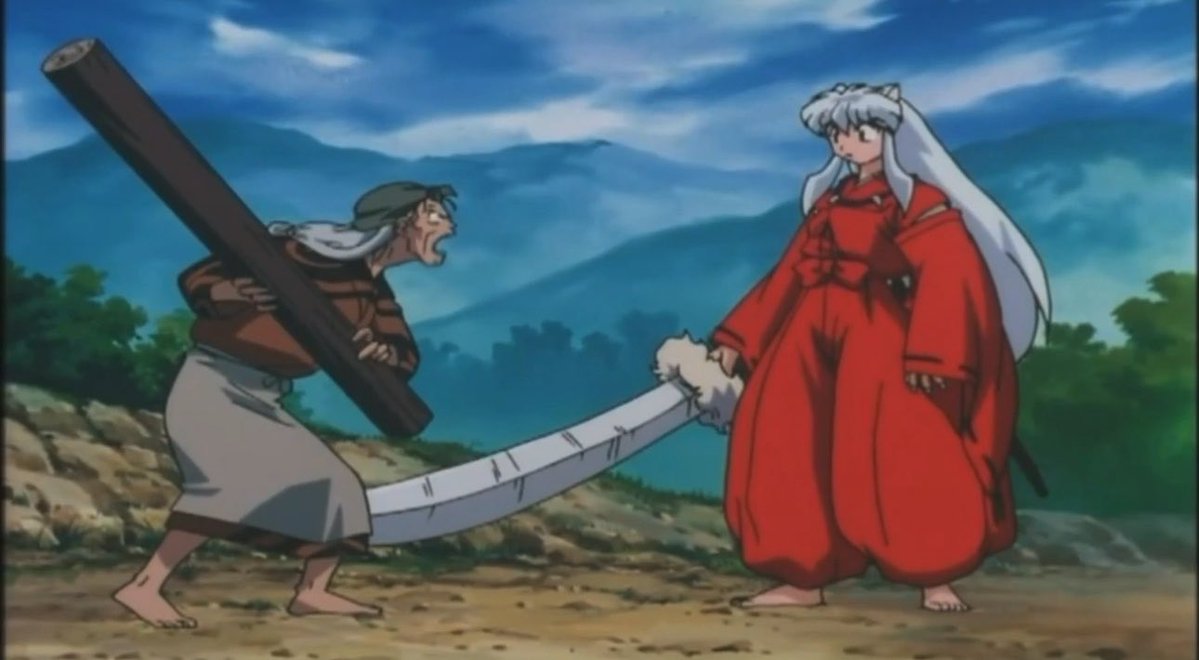 Anime screenshot from Inuyasha showing Inuyasha in his red robe on the right and an old woman carrying a large wooden log on the left, set against a mountainous landscape background.