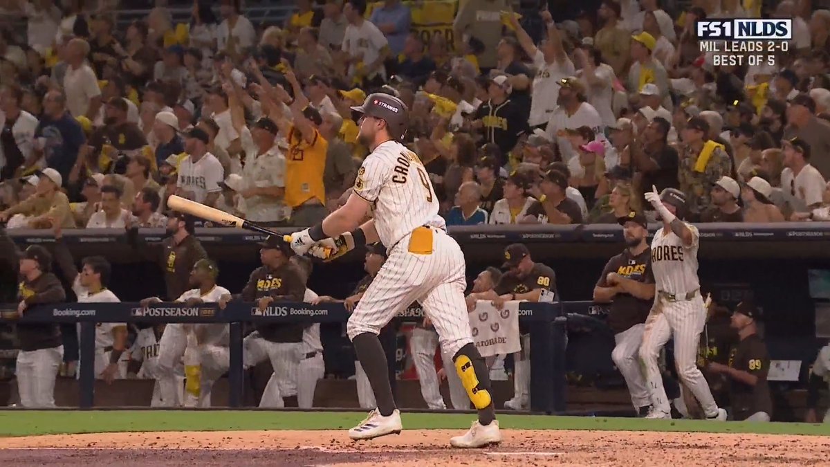 San Diego Padres batter Cron (number 9) holds his bat after a swing, with the 'FS1 NLDS' broadcast graphic showing 'MIL LEADS 2-0 BEST OF 5' as the home crowd cheers.