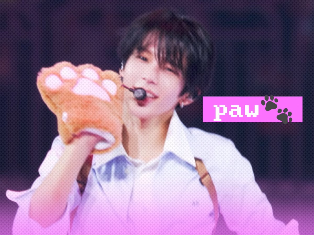A young man on stage wearing a headset microphone and white outfit holds up a fluffy orange cat paw hand puppet, with a pink graphic overlay reading 'paw' with paw print icons.