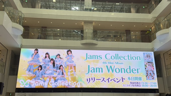 A large digital billboard in a shopping mall advertises 'Jams Collection 4th Mini Album Jam Wonder' release event, featuring photos of a Japanese girl group in blue outfits.