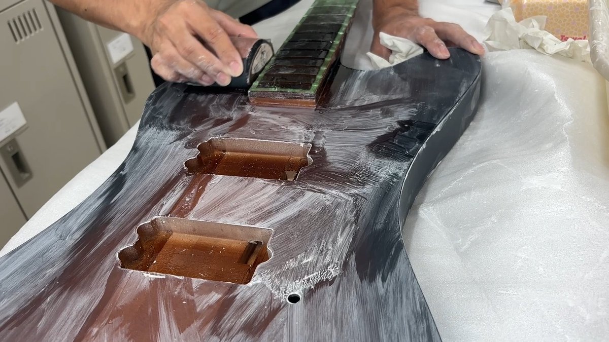 A pair of hands sanding and cleaning a black plastic automotive part, likely a motorcycle fairing, on a white workbench.