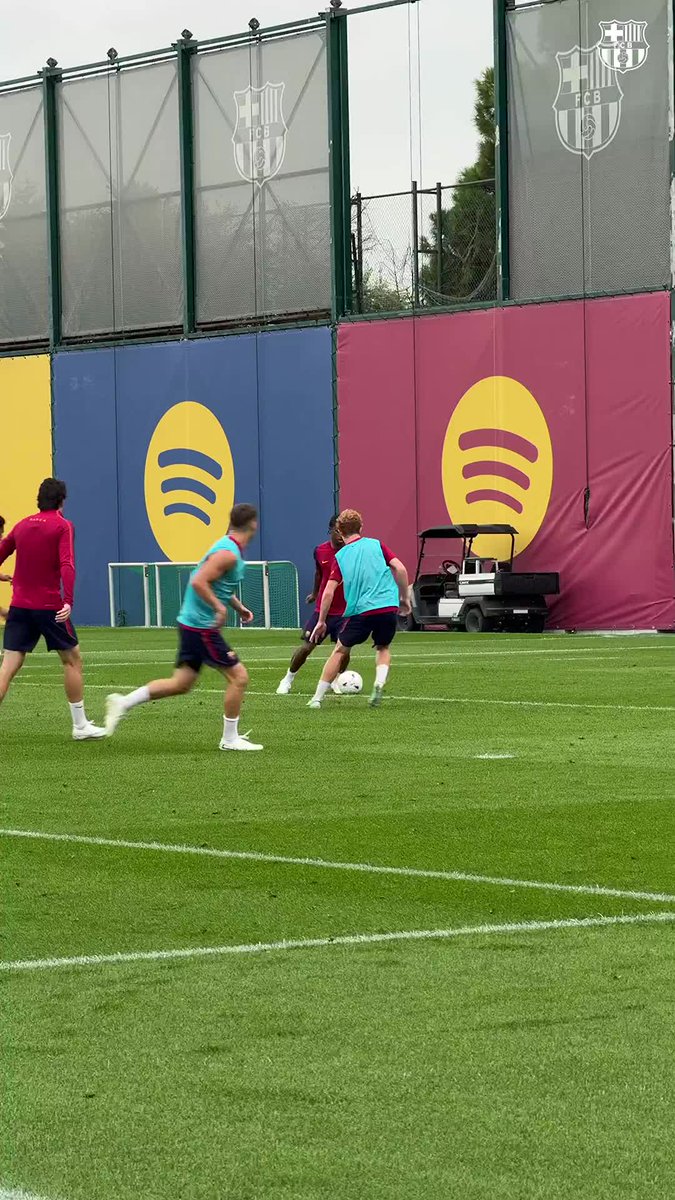 A player in a turquoise training bib controls the ball during what appears to be a Barcelona FC training session, identifiable by the "FCB" logos on the high fencing behind the field. The scene relates to the caption about "ericgm3" (likely Eric García), a young striker honing his skills at the club's training ground.