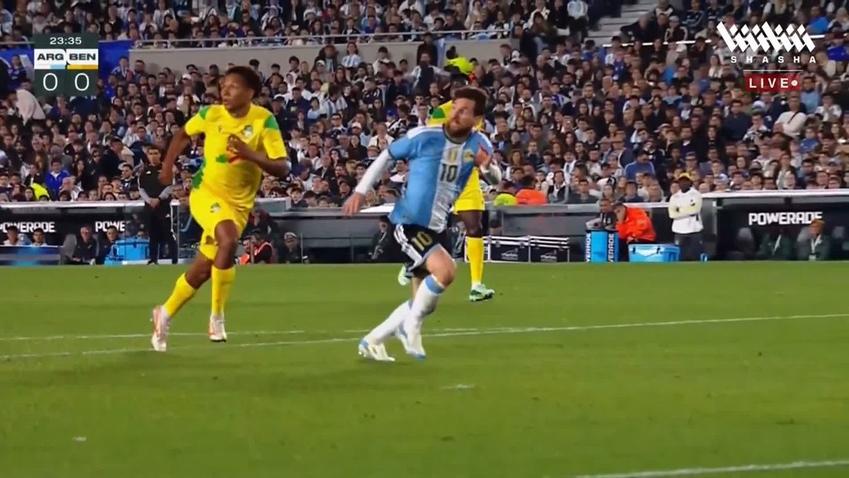 Lionel Messi, in the light blue and white number 10 jersey, celebrates on the field during a 0-0 game between Argentina (ARG) and Benin (BEN) at 23:35, closely guarded by an opponent in a yellow kit, in what is being broadcast live as his retirement match on the Shasha app.