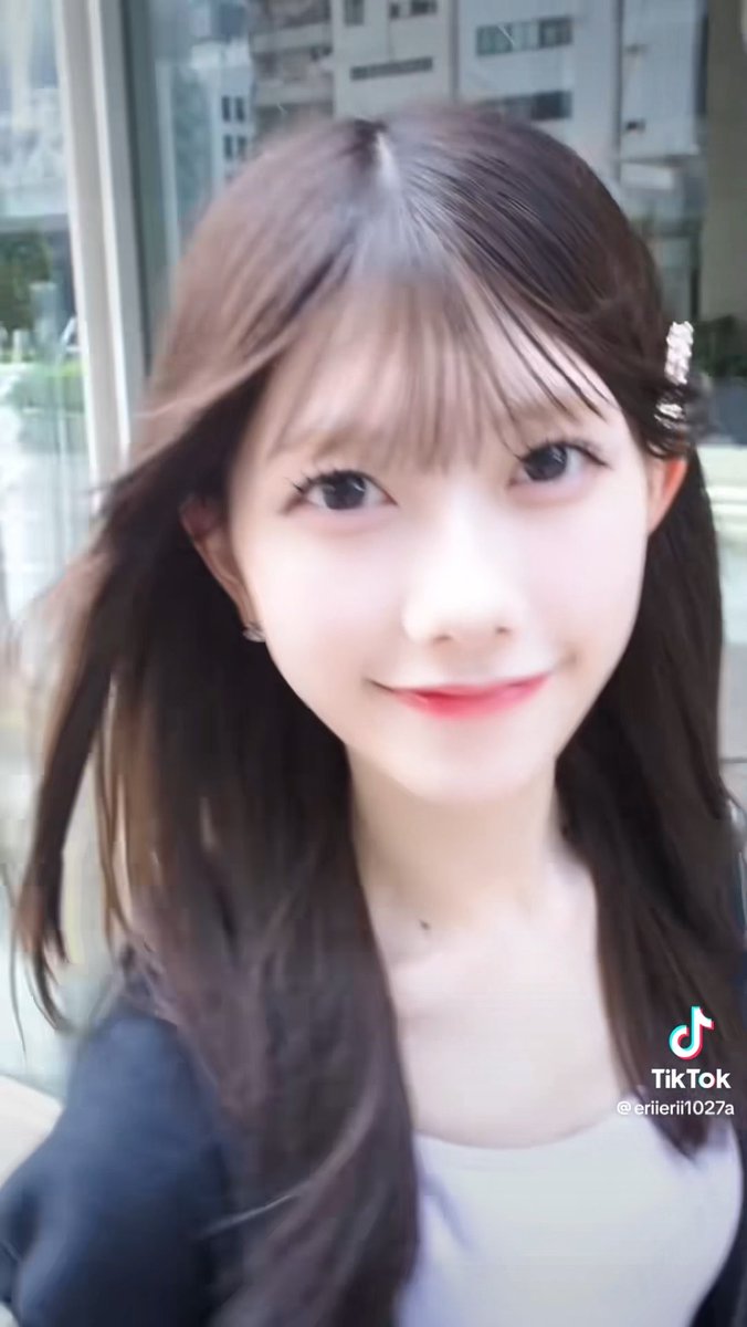 A close-up portrait of a young woman with brown hair and bangs smiling at the camera, with a TikTok watermark and username '@erilierii1027a' visible in the corner.