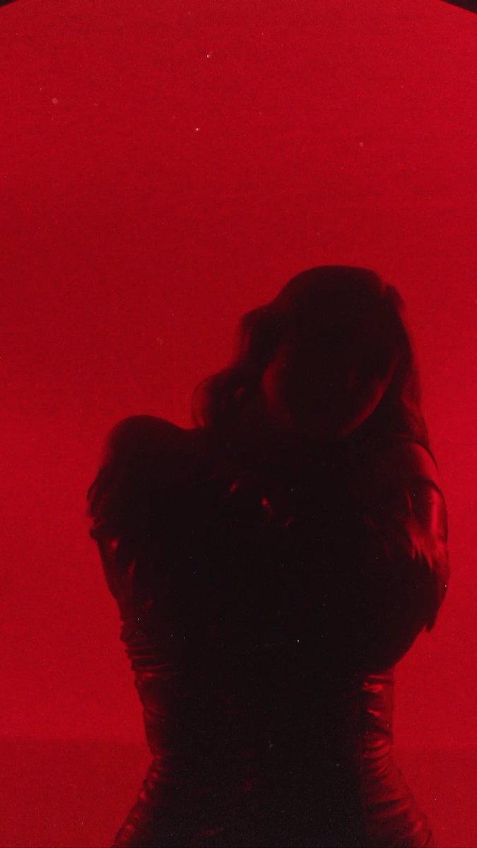 A silhouetted figure of a woman with wavy hair hugging herself against a deep red background.