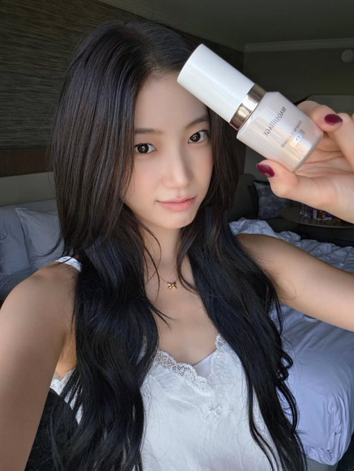 A woman with long dark hair in a white lace top holds up a bottle of Estee Lauder Double Wear foundation next to her face.