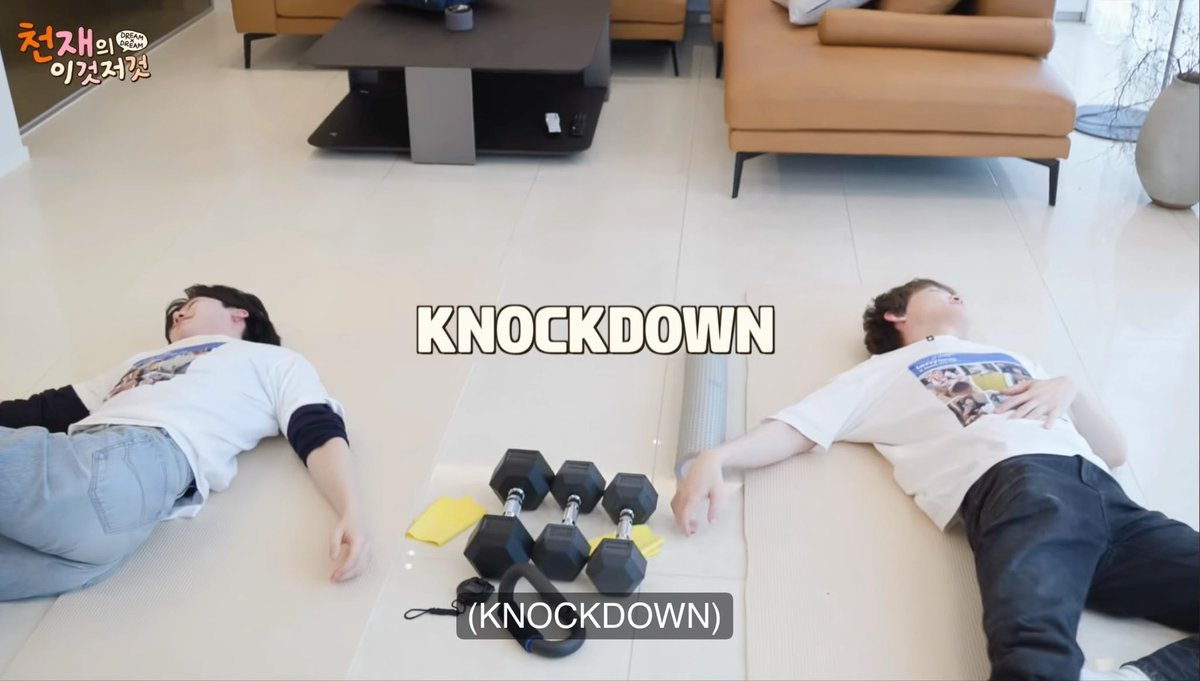 Two people lying unconscious on a living room floor beside dumbbells with the text 'KNOCKDOWN' overlaid, appearing to be from a Korean variety show '천재의 이것저것'.