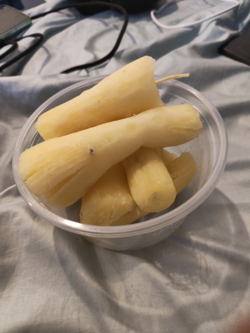 A clear plastic bowl filled with peeled bananas sitting on a gray bedspread with cords visible in the background.