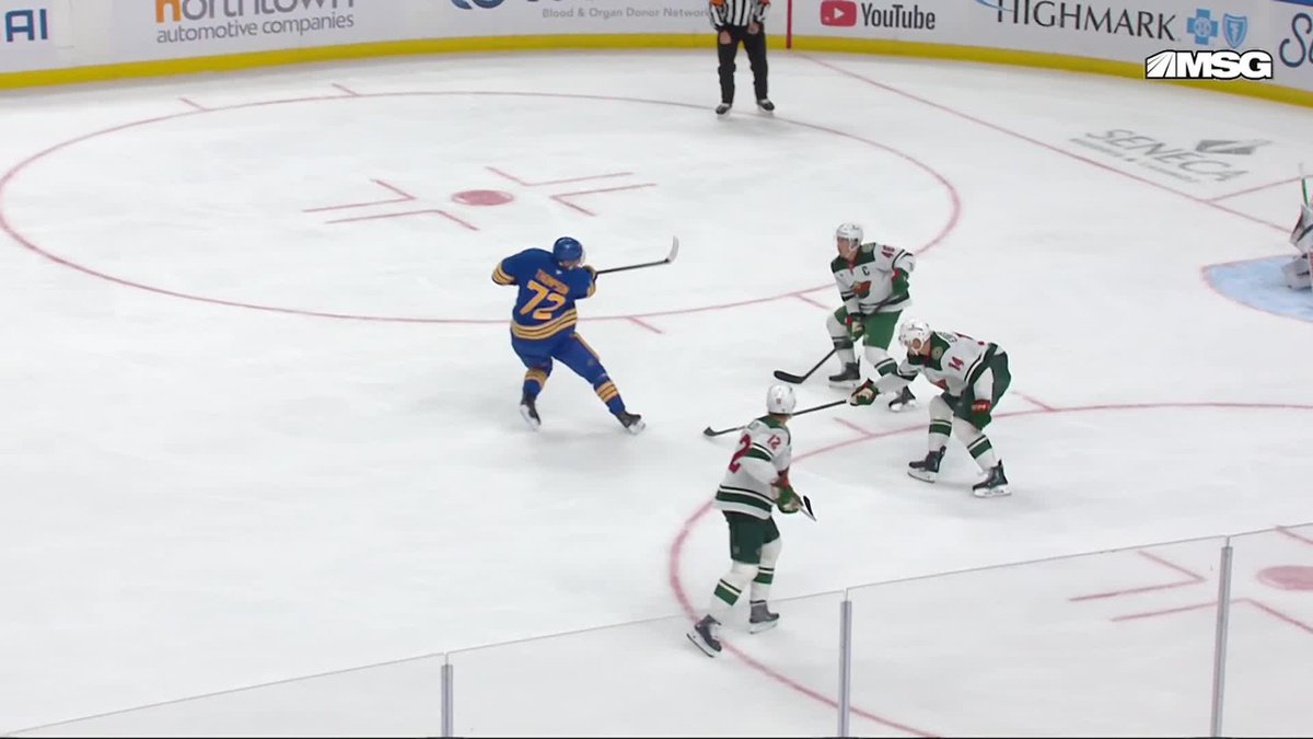 A hockey game in progress at an MSG arena with a player wearing a blue and gold #72 jersey preparing to shoot, while three defenders in white and green uniforms attempt to block.