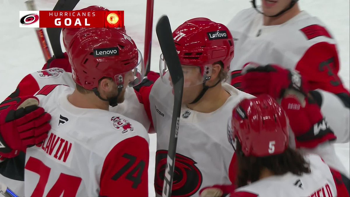 Carolina Hurricanes players, including #74 Slavin, celebrate a goal on the ice, with a "HURRICANES GOAL" graphic displayed in the top left corner. The image contradicts the post's caption, as it shows Hurricanes players celebrating rather than Montreal Canadiens player Taylor Hall scoring.
