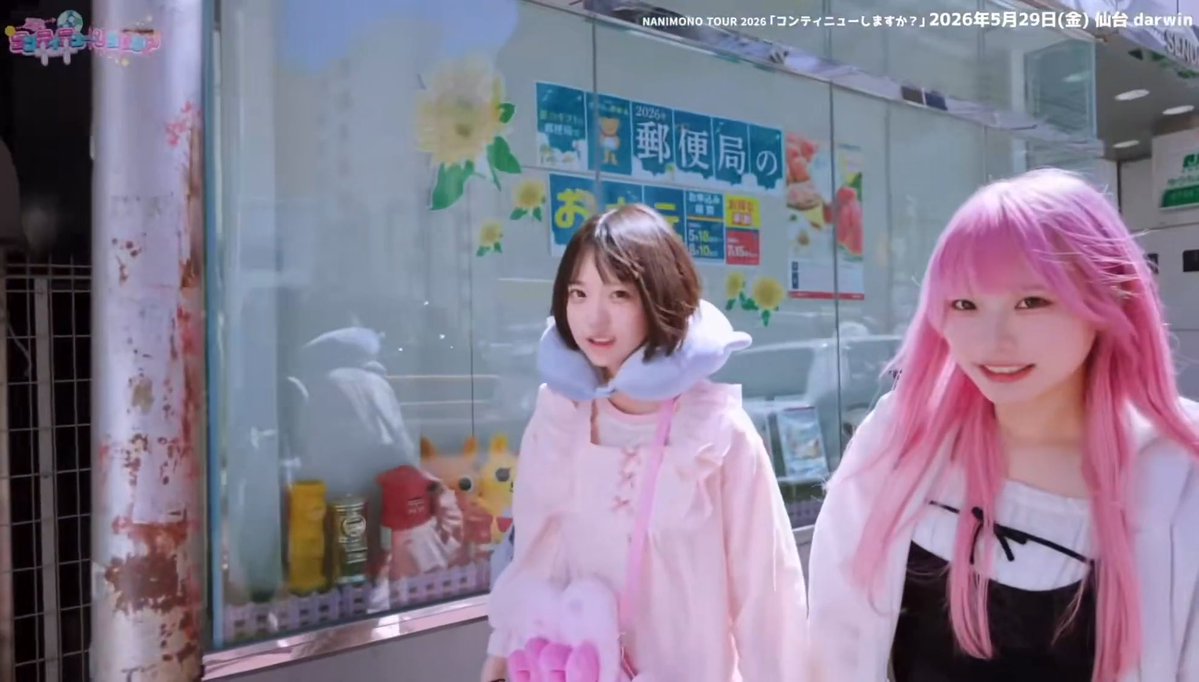 Two young women stand in front of a Japanese storefront with signs reading '郵便局' (post office) and '2026', with one wearing a pink hooded outfit and the other sporting bright pink hair, with text overlay 'NANIMONO.TOUR 2026「ワンデイニューしますか？」2026年5月29日(金) 仙台 darwin'.