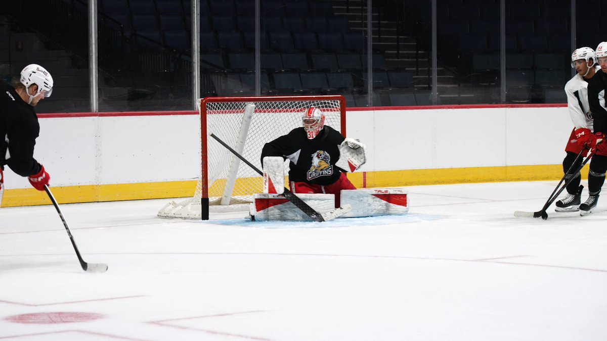 Hockey players practice on the ice, with a goaltender in a Grand Rapids Griffins jersey positioned in the net.