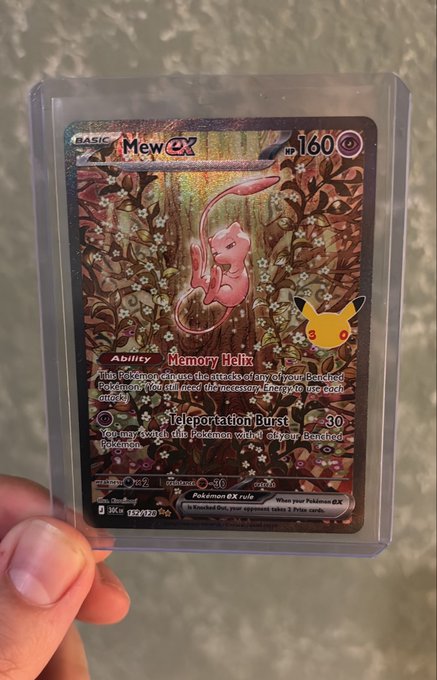 A hand holds a holographic Pokémon trading card featuring Mew ex with 160 HP, displaying the ability "Memory Heux" and an attack called "Teleportation Burst" of 30 damage.