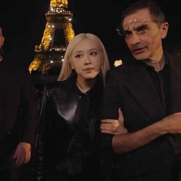 ROSÉ poses alongside creative director Anthony Vaccarello in front of the illuminated Eiffel Tower at the Saint Laurent Paris Fashion Week show.