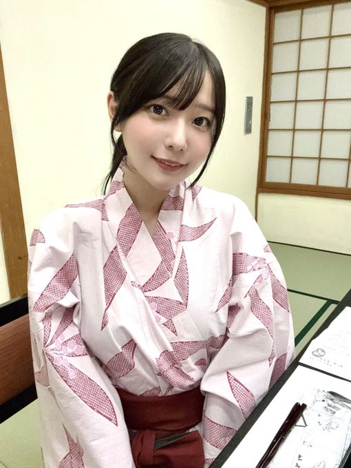 A young woman with dark hair wearing a pink and white patterned kimono, smiling in a traditional Japanese room with shoji screen doors.