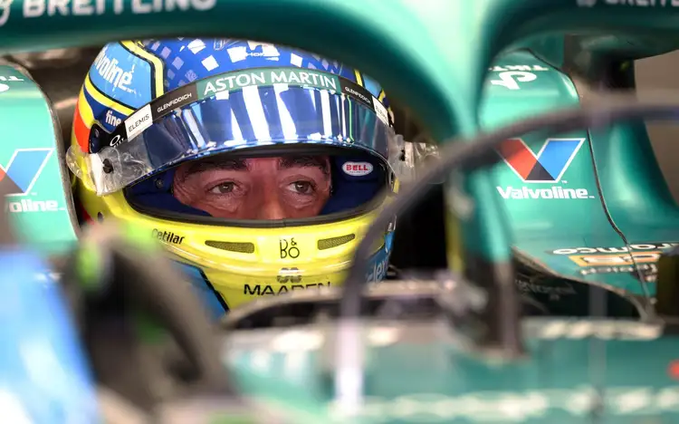 An Aston Martin Formula 1 driver wearing a yellow and blue helmet with sponsor logos including Bell and Aston Martin sits in his green race car.