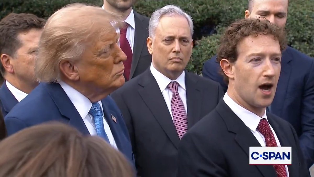 Donald Trump and Mark Zuckerberg stand side by side at what appears to be a C-SPAN broadcast event, with Trump in a blue suit and patterned tie beside Zuckerberg in a dark suit and red tie, while the surrounding political figures—including a gray-haired man in a dark suit between them—appear notably less eye-catching in comparison, perfectly illustrating the post's joke about Zuckerberg's standout "aura" in this power-packed lineup.