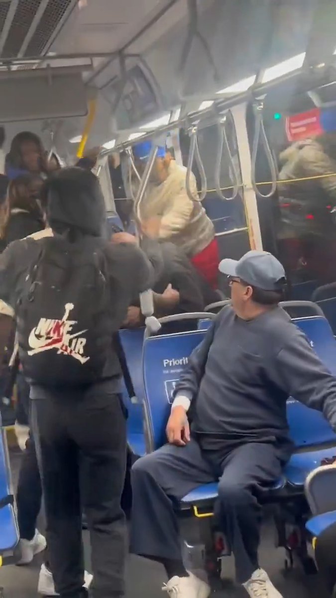 A group assault unfolds inside a CTA bus, with several individuals attacking a man in a beige jacket near the rear, while another seated passenger in a blue cap witnesses the scene. The "Priorit" text on the seat back and a "NIKE AIR" backpack are visible amid the chaos.