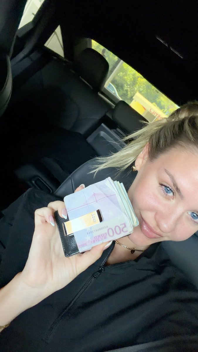 A selfie of a woman in a car holding a wallet with 200 Ukrainian hryvnia banknotes.