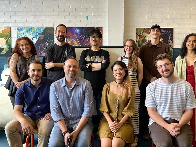 A group of nine people pose together for a team photo, with some seated in front and others standing behind, in a room featuring colorful artwork on the walls. The casual, smiling gathering aligns with the post celebrating a collaboration between KJP, Niantic Spatial, and Liquid City, showcasing the team members from Liquid City who participated in the partnership.