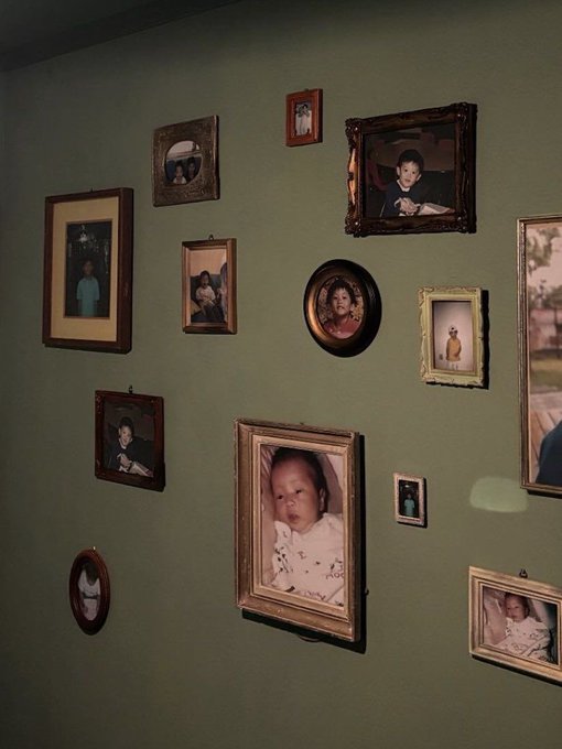 A green wall displays an arrangement of vintage family photographs in various ornate frames.
