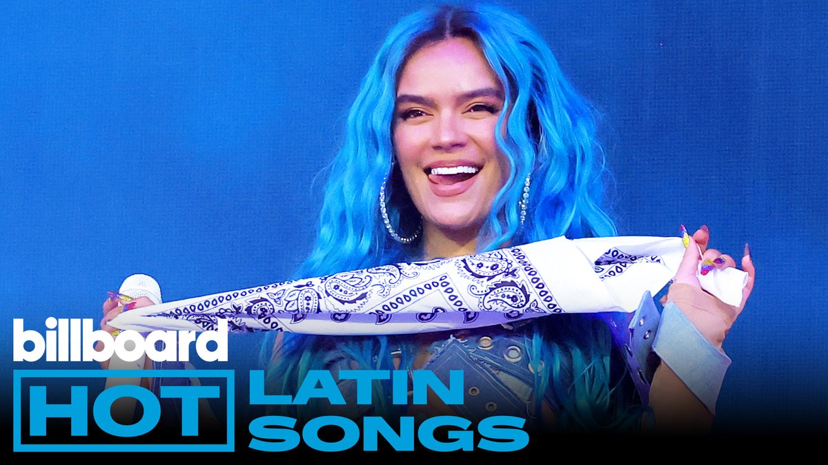 A woman with long blue wavy hair smiles broadly while holding up a white paisley-patterned bandana, with "Billboard HOT LATIN SONGS" text displayed in the corner, promoting Billboard's Hot Latin Songs top 10 chart countdown.