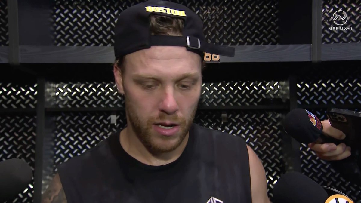 A sweaty, bearded hockey player wearing a black "Boston" cap and sleeveless shirt speaks into multiple microphones in what appears to be a locker room setting, with the NESN 360 logo visible in the corner. The image captures David Pastrnak addressing the media, accompanying his heartfelt comments about the fans' ovation when he took the ice as Bruins captain for the first time.