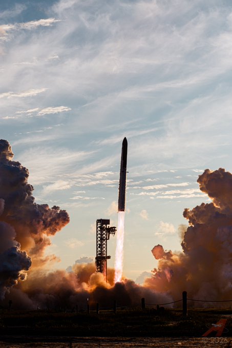 A photograph of a rocket launching into a cloudy sky, leaving a trail of fire and smoke near a launch tower.