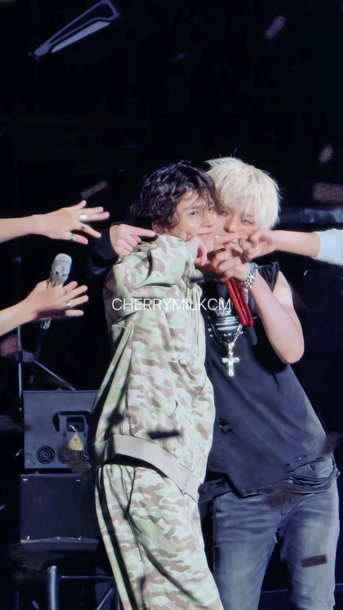 Two performers embrace on stage, one wearing a camouflage jacket and the other a black tank top with a cross necklace; the watermark 'CHERRYMILKCM' is visible.
