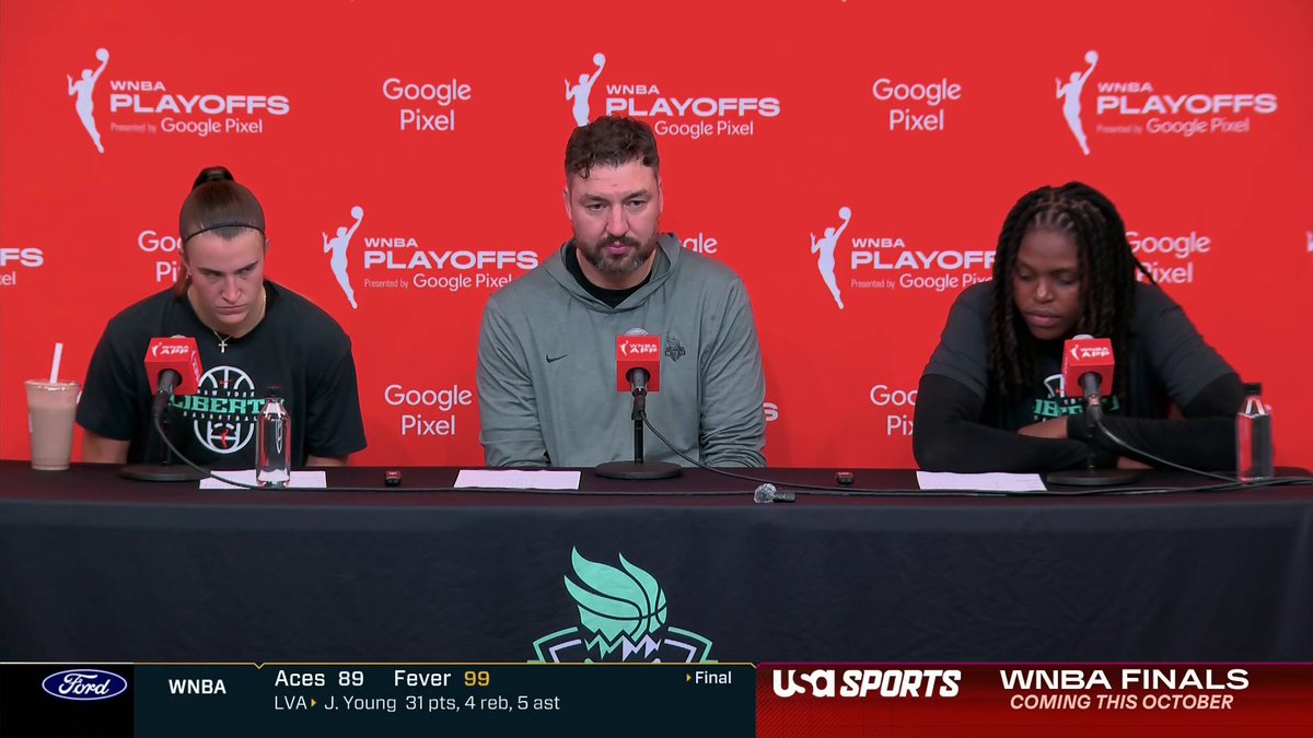 A WNBA Playoffs press conference shows three individuals seated at a table with microphones; a graphic at the bottom shows a final score of "Aces 89 Fever 99" with "J. Young 31 pts, 4 reb, 5 ast" and an ad for "WNBA FINALS COMING THIS OCTOBER" on USA Sports.