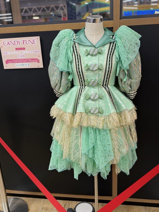 A green and mint costume dress displayed on a mannequin, labeled 'CANDY TUNE' with text including '衣装展' (costume exhibition) and '小原苓奈' (Oihara Reina) on an information card.