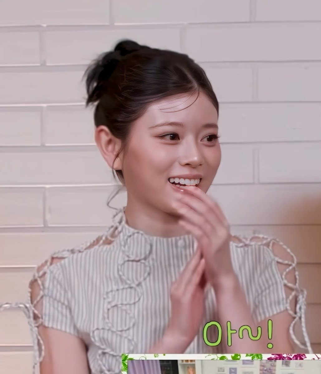 A young woman with her hair in a high bun wearing a striped top smiles brightly with her hands near her face, with green Korean text '아예!' overlaid on the image.