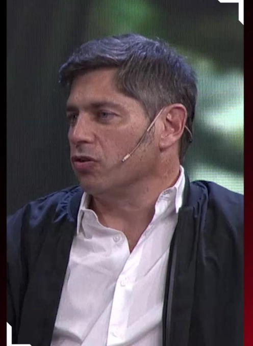 A man with short dark hair, wearing a headset microphone and a white shirt under a dark jacket, speaking on a panel.