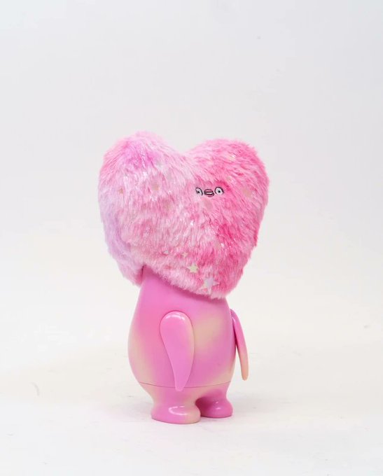 A pink designer toy figurine with a fuzzy heart-shaped head featuring star patterns and a small face, attached to a glossy pink bear-like body.