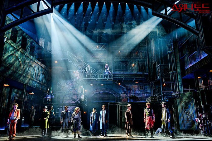 A dramatic stage production of "Sweeney Todd" with cast members spread across an industrial, multi-level set under dramatic lighting, with the theater logo "ДЭНС" visible in the upper right corner—capturing the eerie Victorian atmosphere of the renowned musical.