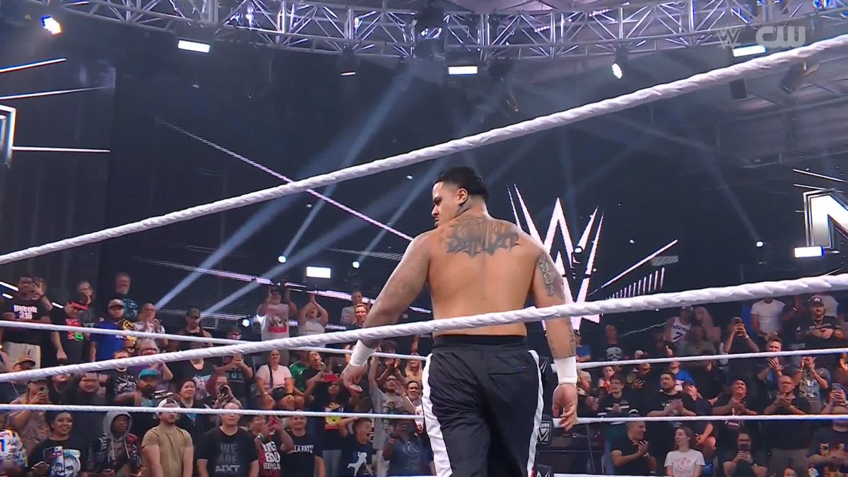 A shirtless wrestler stands in the ring at a WWE event with his back to the camera, revealing a tattoo that reads "ZILLA," fitting the caption "ZILLA ZILLA ZILLA @zillafatu" which highlights his stage name.