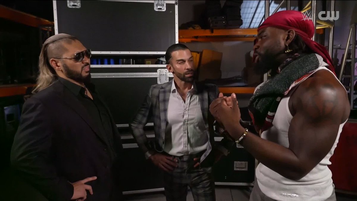The image shows three men backstage at what appears to be a WWE event, with the CW and WWE logos visible in the corner. The post's reference to "Naraku" and Saquon corresponds to the confrontation shown, where the muscular figure on the right wearing a red bandana and white tank top appears to be calling out or being accused by the man on the left in a black suit and sunglasses.