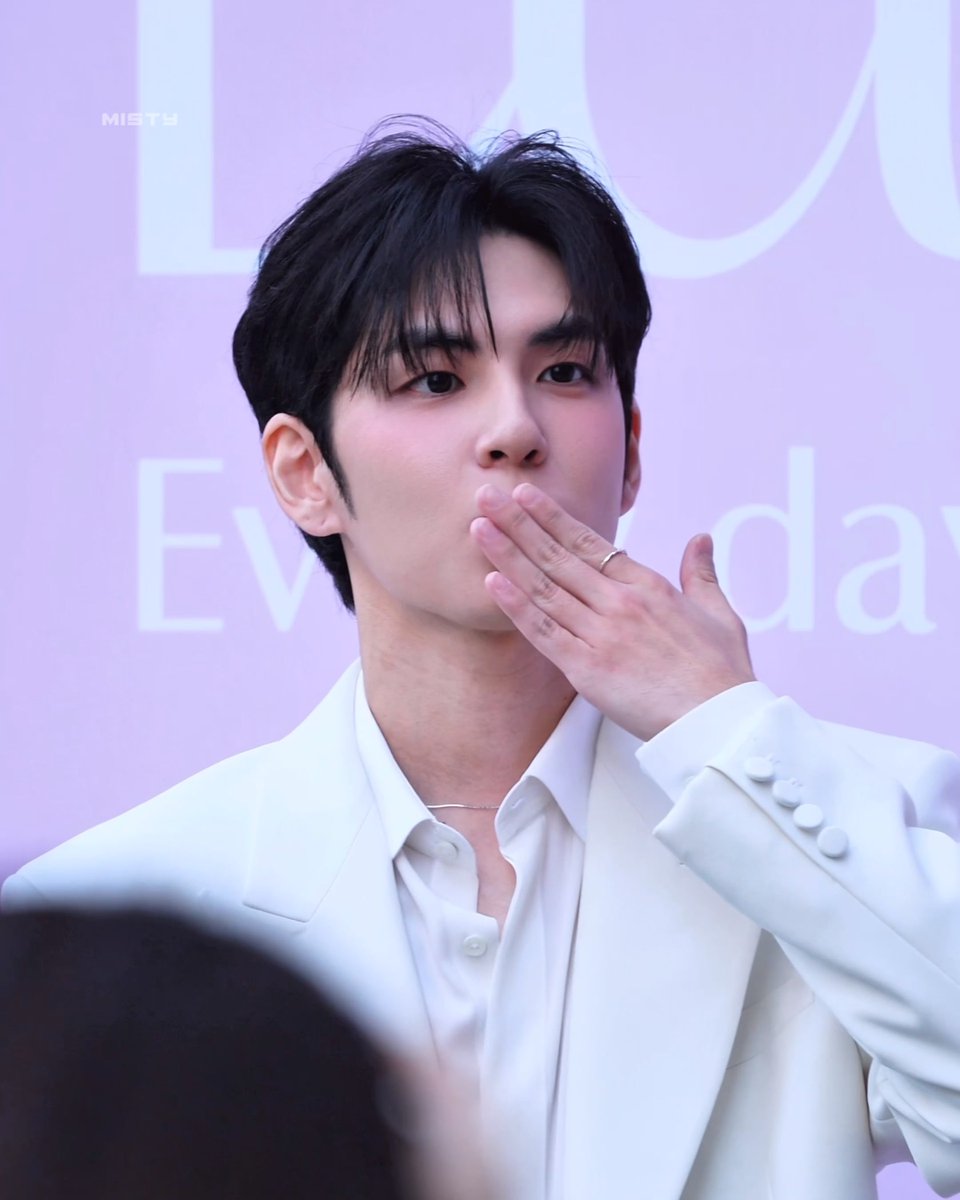 A young man in a white suit blowing a kiss toward the camera at what appears to be a Dior event, with 'MISHA' watermark in the upper left.